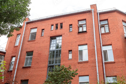 The facade of the old red brick building that was built 100 years ago against the backdrop of the White Sky. Ancient decoration of the building. Restoration of buildings. Old details. Large windows on