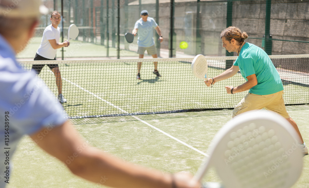 Obraz premium Adult man and elderly man doubles playing against two men in padel tennis on court
