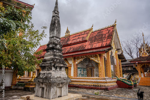 Ancient Stupa and Ornate Temple Exterior with Naga Railings at Wat That Luang Neua, Vientiane, Laos on Cloudy Day photo