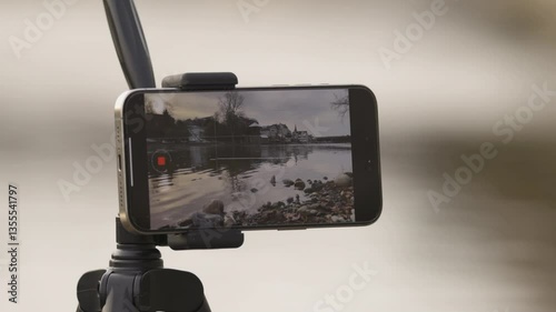 Camera on tripod capturing serene river view with reflections during a cloudy day