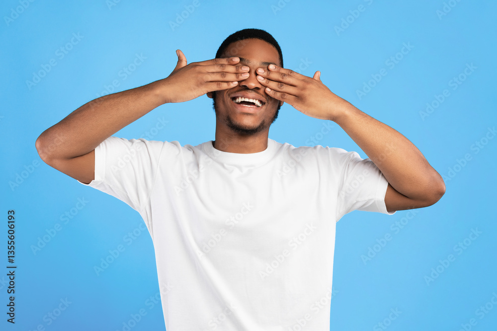 Naklejka premium Cheerful African American Guy Covering Eyes With Hands Standing On Blue Background In Studio. I Don't Look Concept