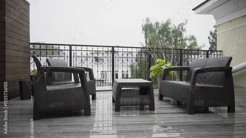 On the open loggia with furniture, heavy rain is pouring. view from the window of the apartment. raindrops fall on a wooden floor on a cloudy day. beautiful view