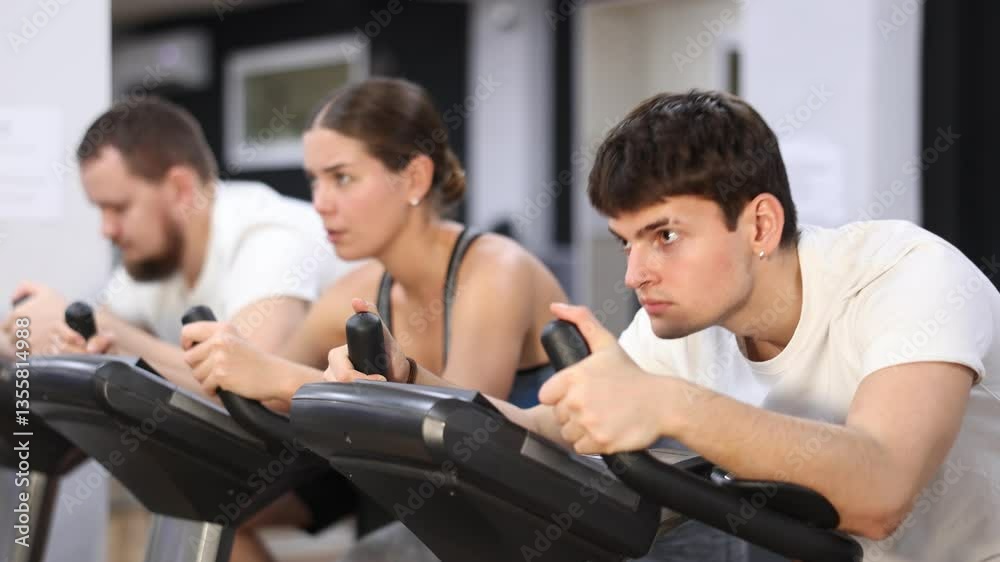 Focused guy is working out on an exercise bike, pedaling hard. Young European during group cycling training Focused guy is working out on an exercise bike, pedaling hard. Young European during group cycling training