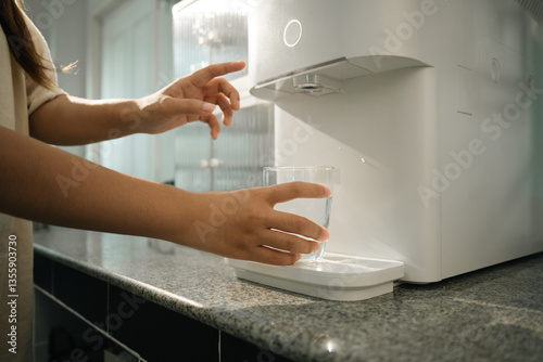 Woman using water purifier marble countertop in a home kitchen. Hydration, health and convenience concept