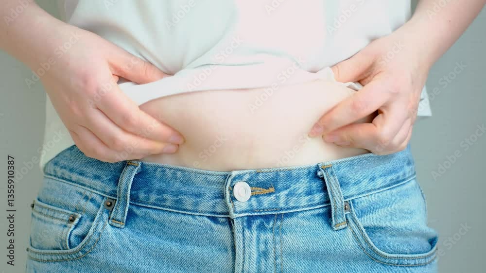 Female hand holds belly on gray background close-up, concept of obesity.