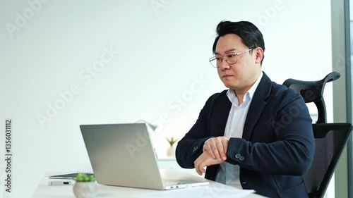 Wallpaper Mural Tired Asian businessman experiencing wrist and arm pain while working on a laptop in a modern office. He rubs his sore wrist and arm, seeking relief. Torontodigital.ca