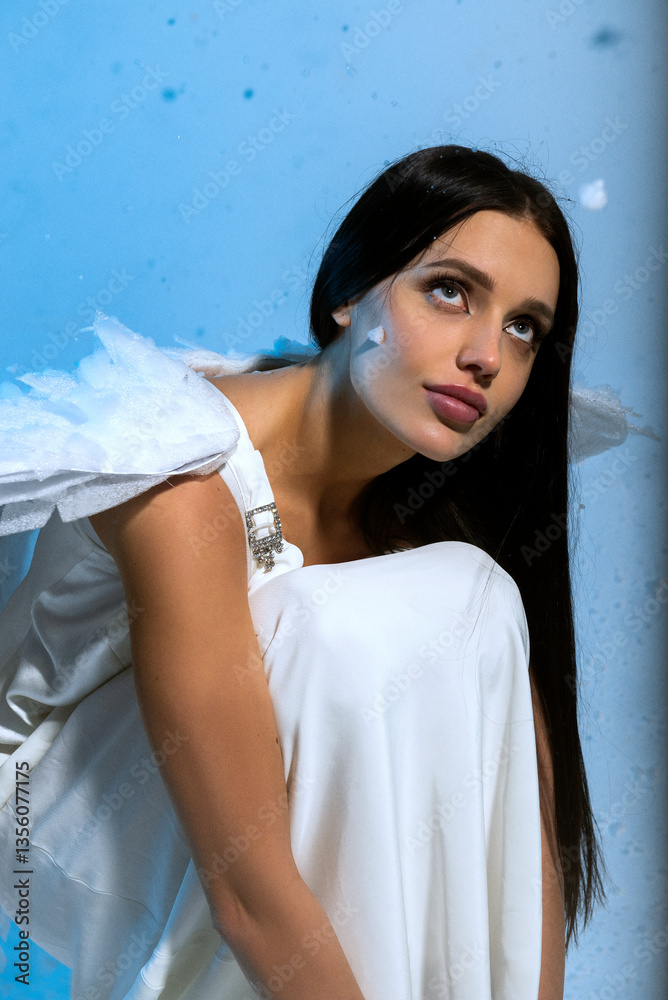 Fototapeta premium Studio portrait of sexy blonde in white long elegant dress and angel wings, she poses sensually 