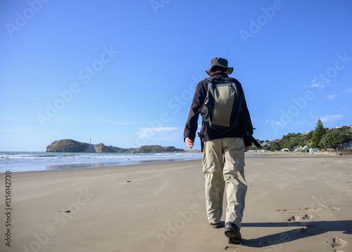 Man walking on Castlepoint beach. Castlepoint lighthouse in the distance. Wairarapa.