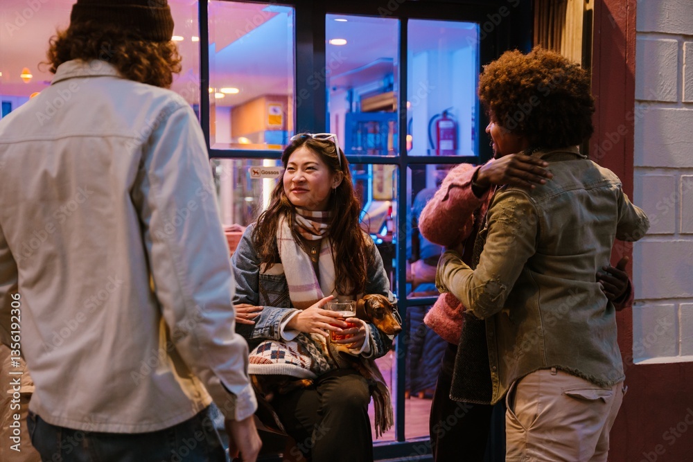Obraz premium A group of multiethnic friends, with an adult Asian woman with a beige scarf holding a dachshund, gathers in front of a cafe featuring colorful lighting and a window. They are talking and hugging.