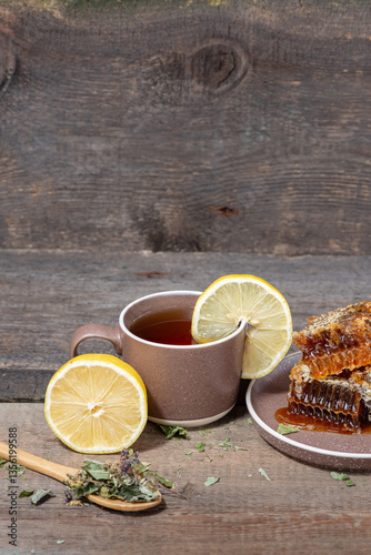 Herbal tea in a ceramic mug, honey in a plate and lemon on a wooden table. Still life