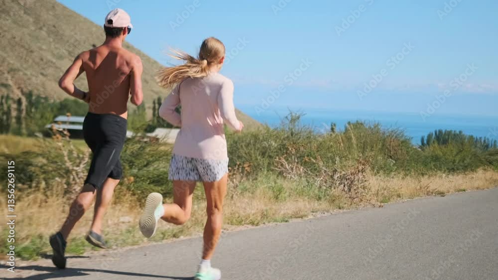 A woman and man, professional athletes, run swiftly along a mountain road, their muscular bodies in sync. The sea stretches ahead, with the rugged landscape perfect for building strength and endurance A woman and man, professional athletes, run swiftly along a mountain road, their muscular bodies in sync. The sea stretches ahead, with the rugged landscape perfect for building strength and endurance