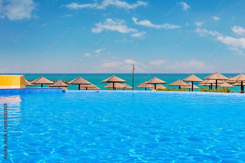 Luxury hotel pool in Sharjah with crystal-clear water, surrounded by elegant sun loungers. Stunning sea views and a golden sandy beach create a relaxing atmosphere under the bright daytime sun.