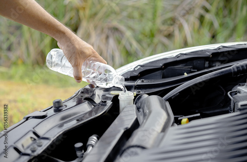 Driver's hand pouring or refilling water into the windshield washer tank inside the car hood. Checking and refilling the car's radiator.