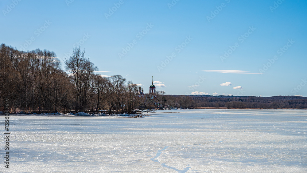 Fototapeta premium The lake shore with frozen water, bare trees in sunny day at early spring. 