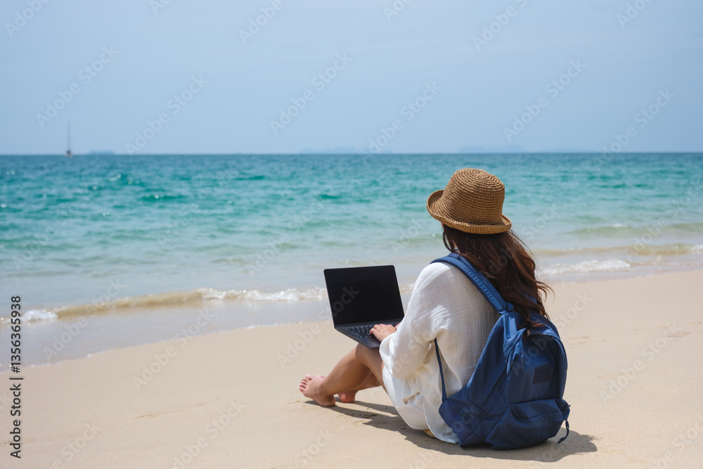 A female traveler using and working on laptop computer while sitting on the beach A female traveler using and working on laptop computer while sitting on the beach