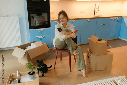 Woman using smartphone for online shopping in a newly renovated kitchen with moving boxes and a dog photo