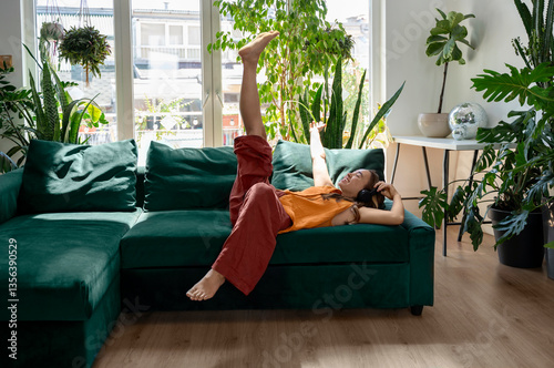 Happy young woman relaxing on a green couch in a plant-filled living room
