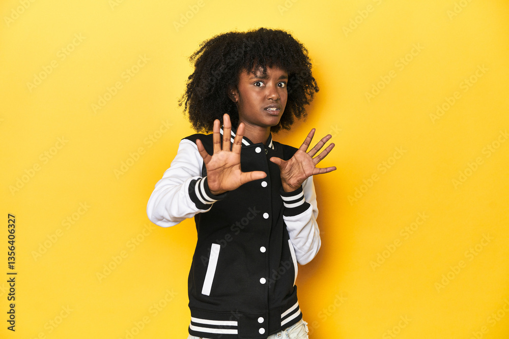 Obraz premium Teen girl in baseball jacket, yellow studio background being shocked due to an imminent danger