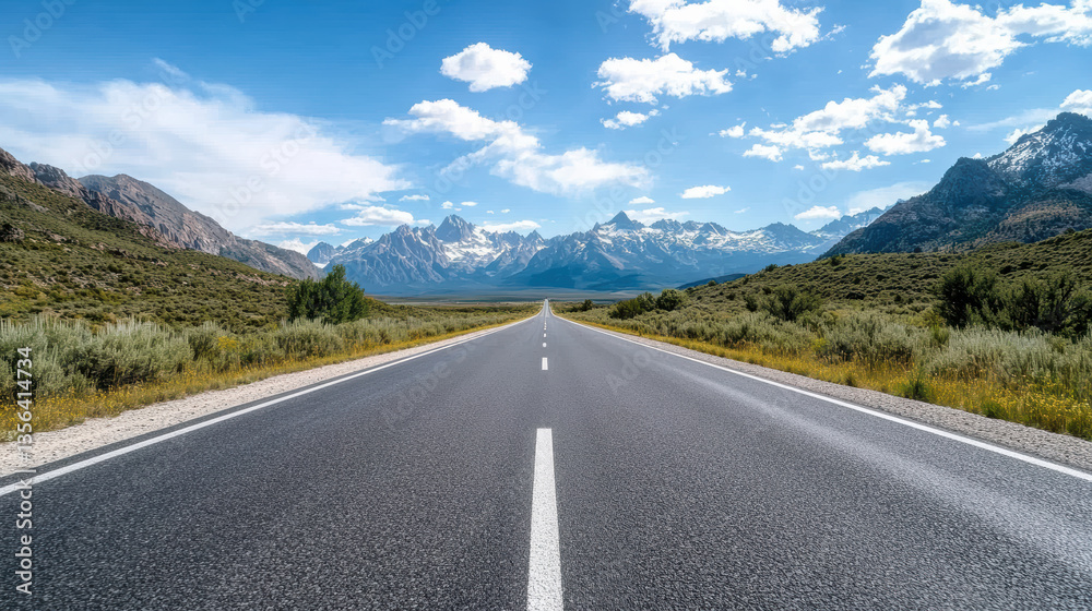 Naklejka premium scenic view of long, open road stretching towards majestic mountains bright blue sky