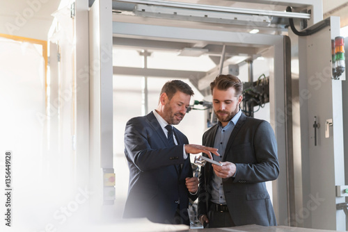 Two businessmen having a meeting in a factory examining workpiece