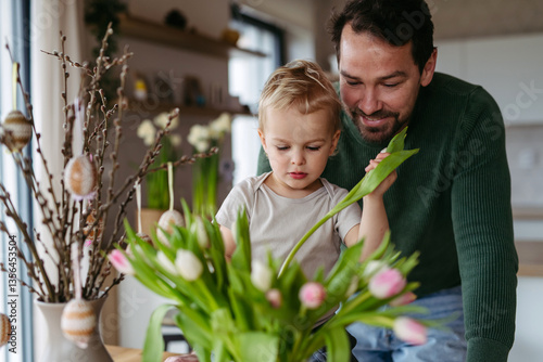 Father and little son arranging tulips in a vase.