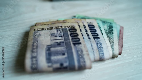 Bangladeshi Banknotes on Wooden Surface, A stack of various denominations of Bangladeshi banknotes fanned out on a wooden surface