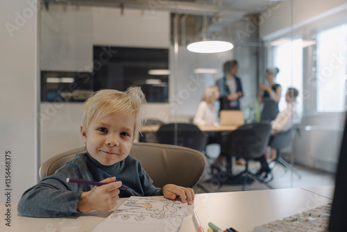 Portrait of smiling boy painting in office with business team having a meeting