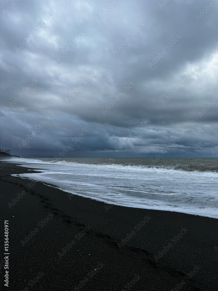 Footprints on black sand beach under stormy clouds