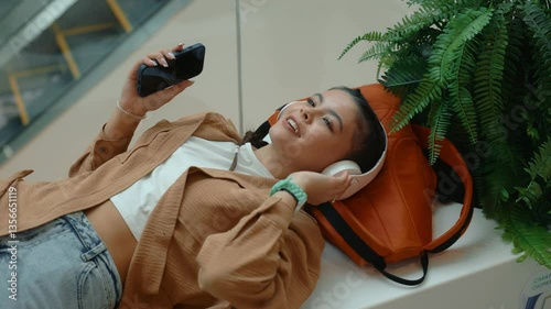 Teenage girl listening to music using smartphone resting in shopping mall