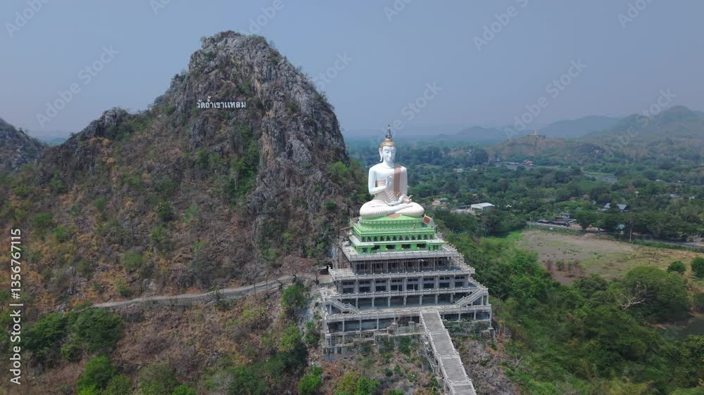 Wide-angle drone shot from left to right showing the surrounding area and the large Buddha statue at Wat Tham Khao Laem, Kanchanaburi, Thailand. Wide-angle drone shot from left to right showing the surrounding area and the large Buddha statue at Wat Tham Khao Laem, Kanchanaburi, Thailand.