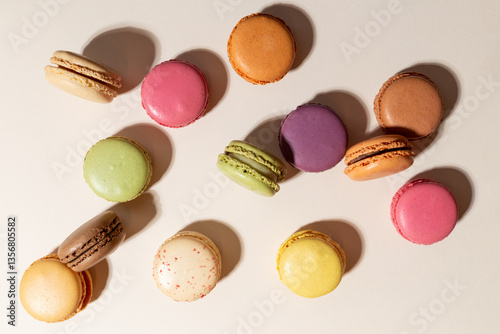 Bunte Macarons stehend und liegend, chaotisch geordnet auf dem beigen Hintergrund. Farbenfrohe, fröhliche Kombination.