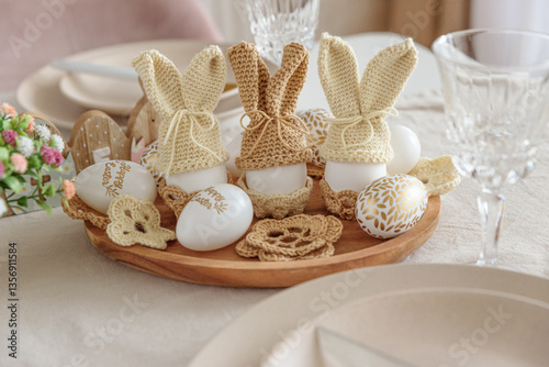 Festive Easter table setting with several Easter bunny made from egg and knitted ears on wooden plate. Easter celebration concept