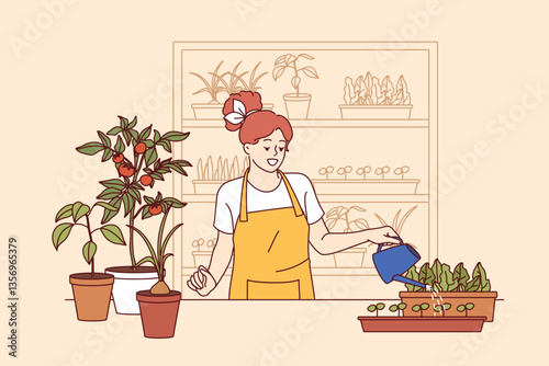 Woman florist grows house plants, uses watering can, standing near table and shelves with houseplants. Young girl florist enjoys own work, dressed in apron to avoid stains on clothes