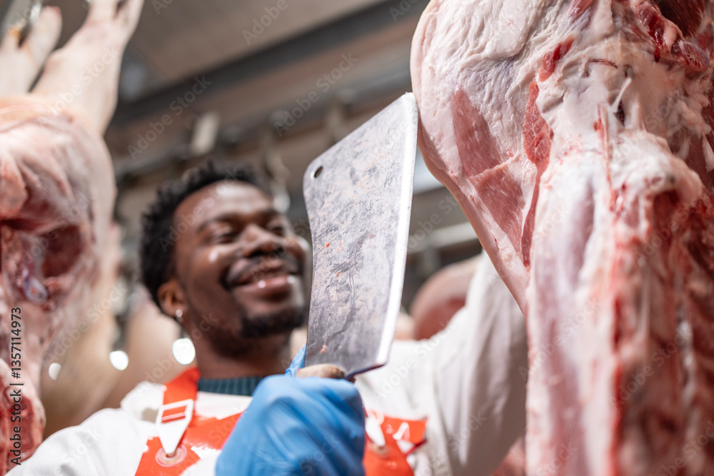 Obraz premium Smiling butcher working in slaughterhouse cutting hanging raw meat.