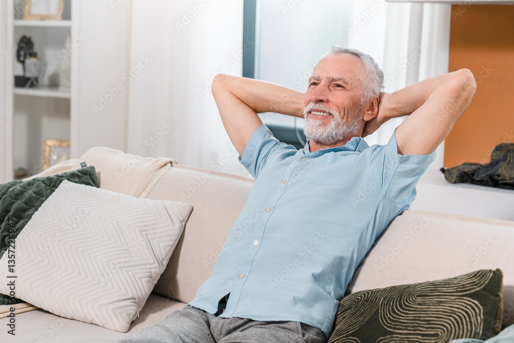 Fototapeta premium Smiling retired caucasian senior mature middle aged man relaxing on sofa in the living room at home, enjoying sunny afternoon. Lifestyle happy retirement concept