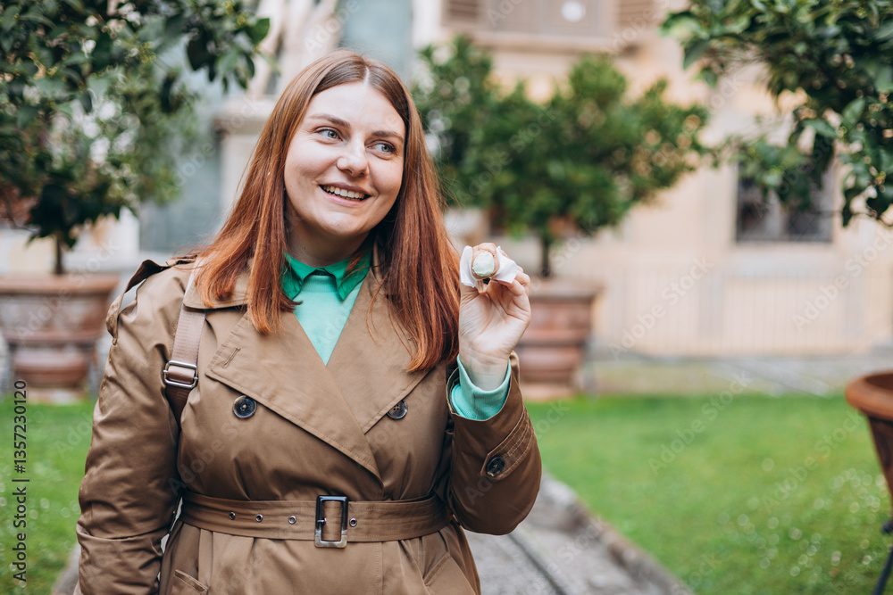 Happy 30s woman holding Sicilian cannolo tube pastry filled with cream outdoors. Travel, Italy, food and holidays concept. Young woman eating traditional delicious cake cannoli, Traveling Europe