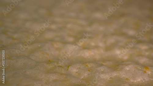 Beer fermentation process in a cold chamber. The golden liquid is actively fermenting, with foam gently swirling and bubbling on the surface, creating a lively, dynamic effect. The metal tank and frot photo