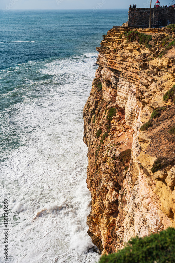 Edge of a rough cliff facing big waves in Nazare, Portugal