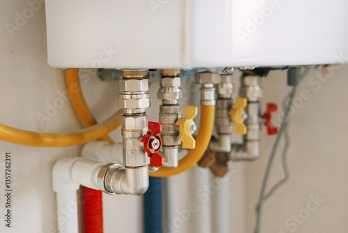 Close-up view of water heater pipes and valves in a utility room, featuring colorful connectors and tubes. Essential components for heating system maintenance and operation. Gas boiler taps.