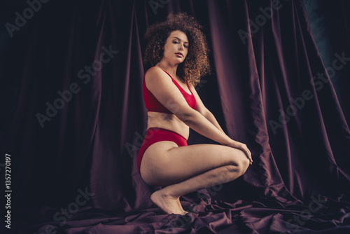 Young woman in bold red lingerie posed against purple fabric backdrop embracing natural beauty and feminine confidence
