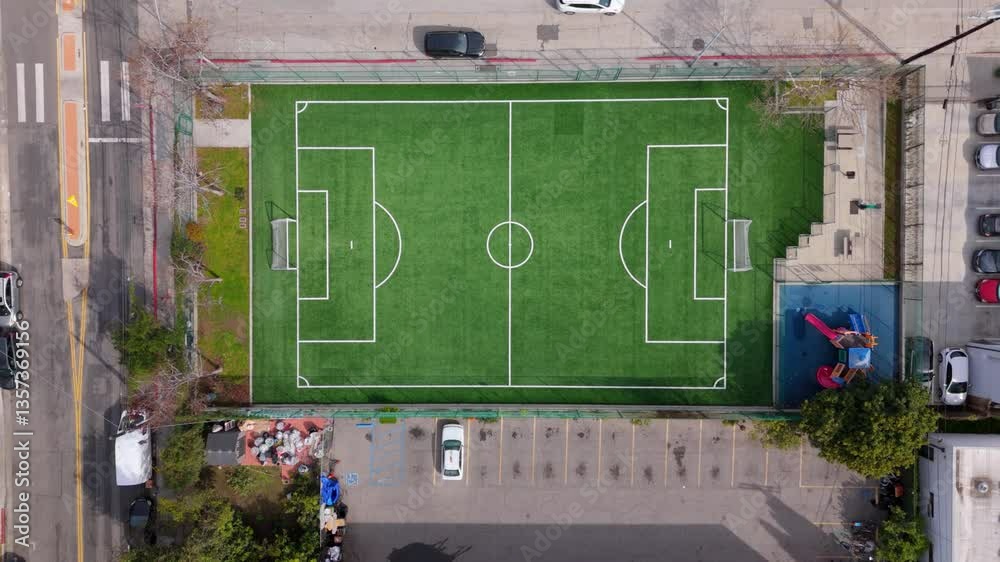 Aerial ascending shot over urban soccer green field with playground, parking lot, and street