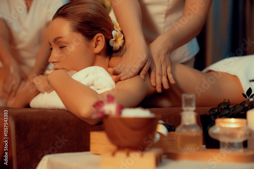 Caucasian couple customer enjoying relaxing anti-stress spa massage and pampering with beauty skin recreation leisure in warm candle lighting ambient salon spa at luxury resort or hotel. Quiescent