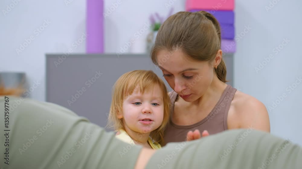 A touching scene of a mother and daughter holding each other warmly in a gym, with the toddler playfully interacting with a woman working out in the background A touching scene of a mother and daughter holding each other warmly in a gym, with the toddler playfully interacting with a woman working out in the background