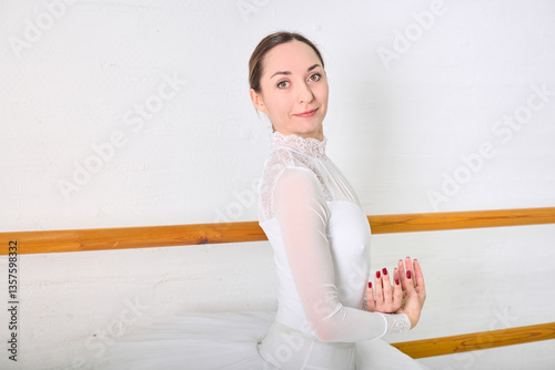 Bild auf Leinwand Young female ballerina with dark hair in white costume poses gracefully in bright studio
