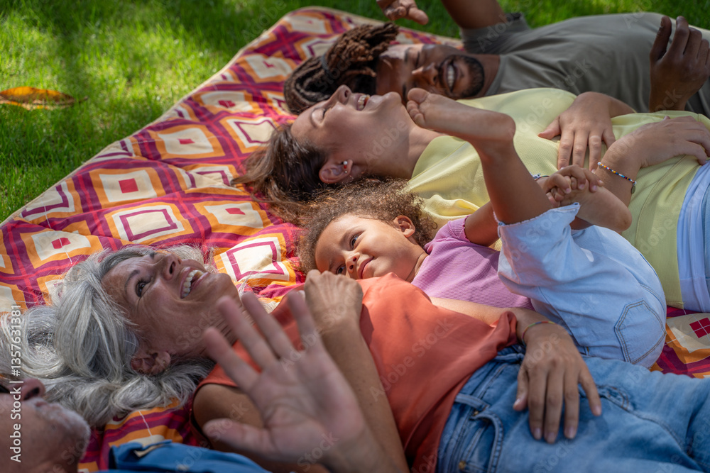 Fototapeta premium A happy multi-generational and diverse family relaxing together on a picnic blanket in a park. Concept of family bonding, love, legacy, and quality time across three generations.