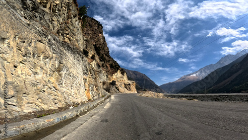 Driving down an empty road with a view of mountains in the distance and cloudy sky. 