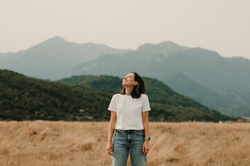 A woman stands peacefully in a vast field, gazing at the majestic mountains in the serene embrace of nature