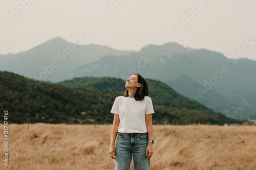 A woman stands peacefully in a vast field, gazing at the majestic mountains in the serene embrace of nature