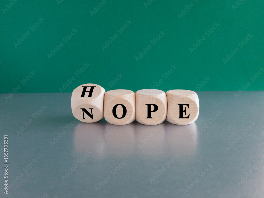 Hope or nope symbol. Turned a wooden cube and changes the word 'nope' to 'hope'. Beautiful green background, gray table. Business and hope or nope concept.