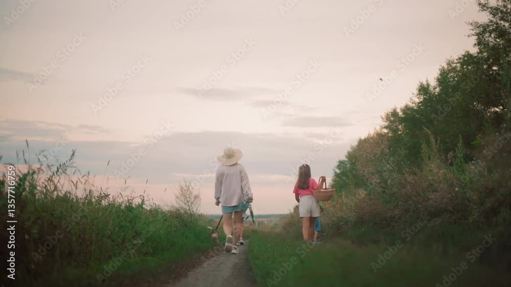 Back view of family walking home along a dirt path at sunset, with a bird flying overhead, two women in hats walk with a dog on a leash, while a young girl carries a basket and a boy plays Back view of family walking home along a dirt path at sunset, with a bird flying overhead, two women in hats walk with a dog on a leash, while a young girl carries a basket and a boy plays